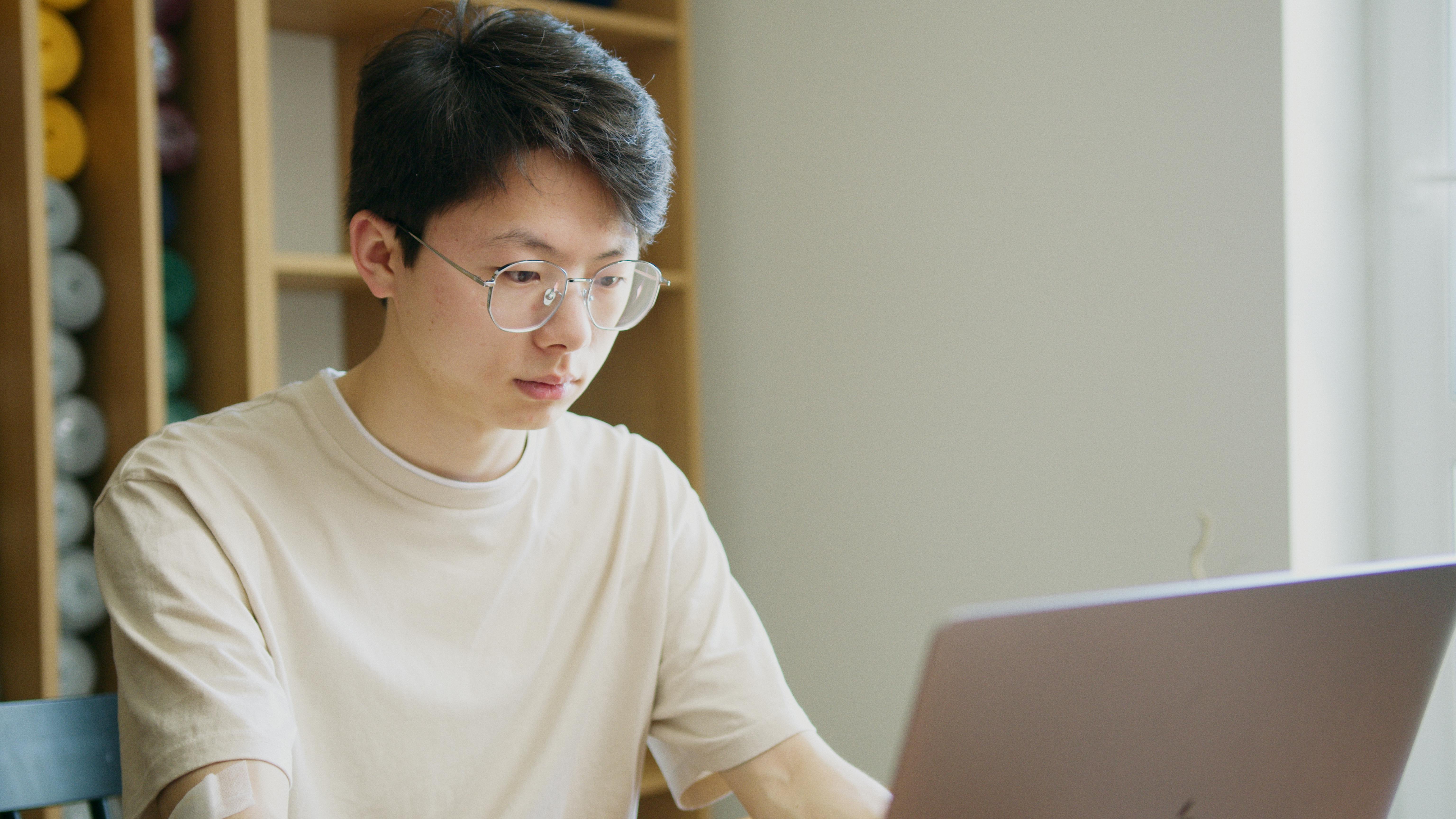 一位戴眼镜的年轻人在室内专注使用笔记本电脑